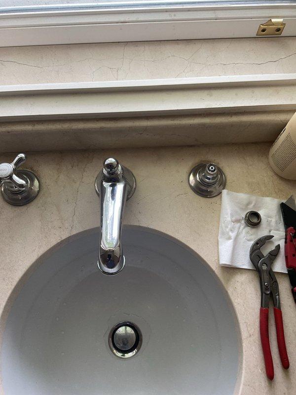 Completed faucet installation in kitchen and bathroom. Kitchen work included installing new chrome faucet assembly with dual handles and integrated soap dispenser on white counter surface. Bathroom service involved faucet replacement on round gray basin with updated single-handle chrome fixture. Removed old hardware, installed new mounting brackets, connected water supply lines, and tested both fixtures for proper operation and leak-free performance.