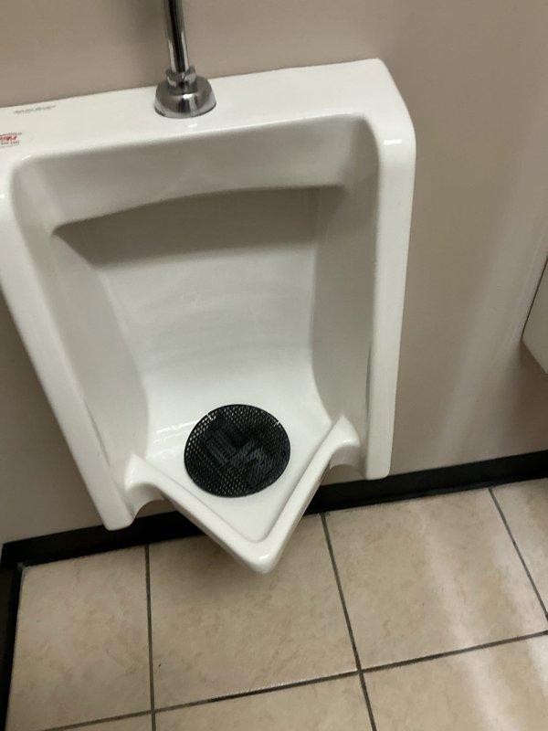 Responded to complaint of urinal backing up in commercial shop restroom. Upon inspection, found wall-mounted porcelain urinal with drainage issues. Cleared obstruction from drain line and verified proper flow through flush valve system. Tested fixture operation to confirm complete drainage and proper function of chrome flush valve assembly. Unit restored to normal working condition.