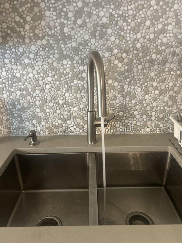 Successfully installed a Kohler Rodean single-handle pull-down kitchen faucet with high-arc spout and spray functionality in brushed stainless steel finish. The faucet was mounted to a modern double-basin composite sink with proper connections verified and tested for leaks, with water flow confirmed operational upon completion.