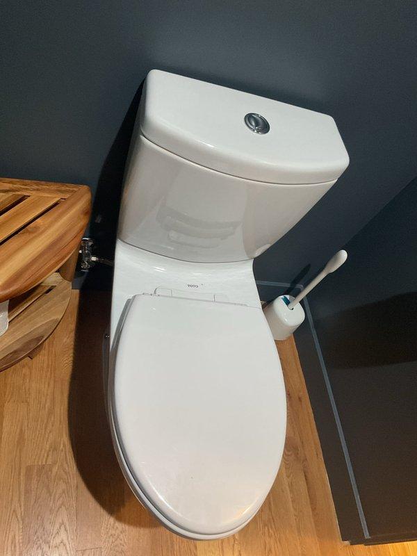 Responded to service call for odor complaint related to toilet fixture. Upon arrival, performed thorough inspection of TOTO two-piece toilet with dual-flush mechanism. Examined wax ring seal, flange connection, and trap for potential sources of sewer gas infiltration. Verified proper operation of flush mechanism and water seal in bowl. Documented existing bathroom conditions including modern one-piece toilet installation with corner storage area containing cleaning supplies. No immediate mechanical failures or leaks detected during visual inspection.