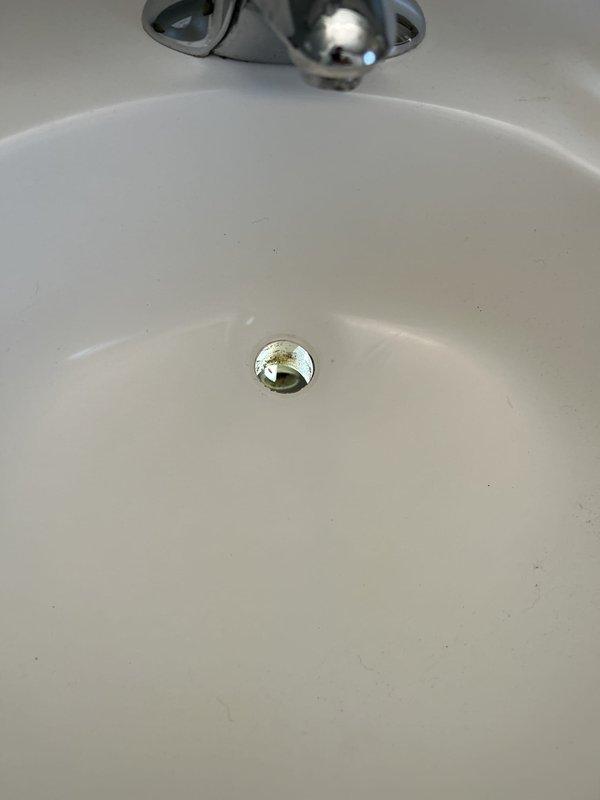 Responded to service call for multiple plumbing issues including dishwasher leaking from bottom due to suspected clogged valve, bathroom sink with minor leak at drain assembly, and toilet replacement with customer-supplied fixture. Inspected bathroom sink P-trap and drain connections beneath cabinet, identifying source of leak at flexible accordion-style tubing connection. Documented existing plumbing configuration including white PVC P-trap assembly, chrome shut-off valves, and black braided supply lines for future reference during repairs.