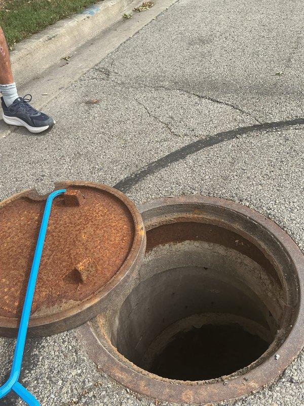 Performed camera inspection of underground sewer line accessed through exterior manhole. Removed rusted manhole cover to gain access to the drainage system and deployed camera equipment into the main line. Inspection focused on evaluating the condition of the sewer lateral and identifying any blockages, root intrusion, or structural deficiencies in the underground piping system running alongside the building's foundation near the downspout drainage area.