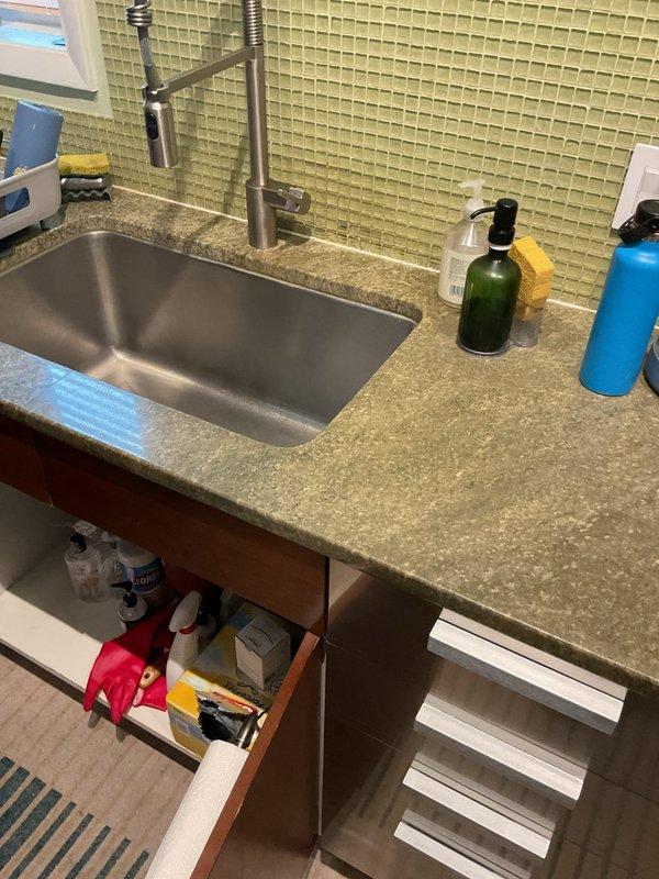 Responded to kitchen sink drainage issue where water was backing up after initially draining. Upon inspection, identified clog in the drain line beneath the sink. Deployed motorized drain cleaning machine with cable auger to clear the obstruction. Successfully removed blockage from the line, restoring proper drainage flow. Tested sink operation to confirm water now drains freely without backup. Plumbing system beneath sink, including garbage disposal and PVC drain assembly, functioning normally upon completion.
