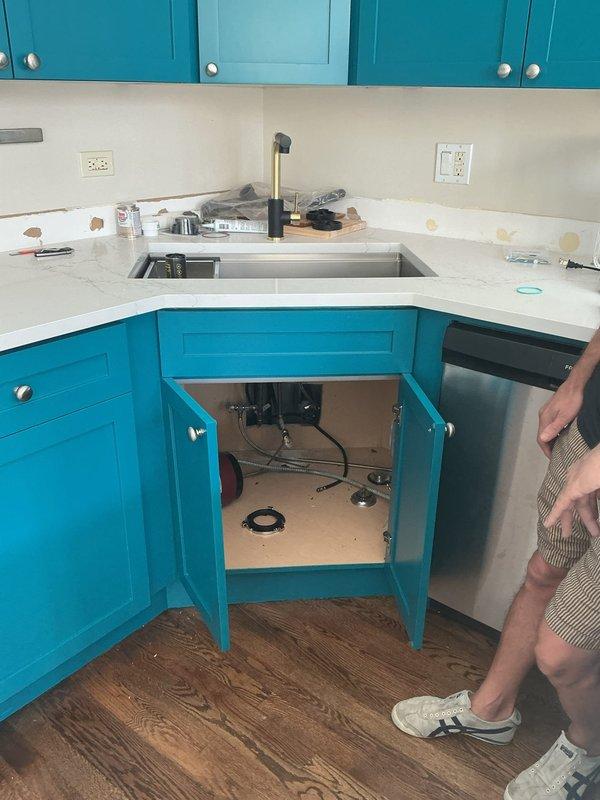 Completed kitchen faucet and under-sink plumbing service at residential property with turquoise cabinetry. Installed new pull-down faucet assembly at stainless steel undermount sink, verified proper mounting and water supply connections, and tested garbage disposal unit and drain connections to ensure leak-free operation.
