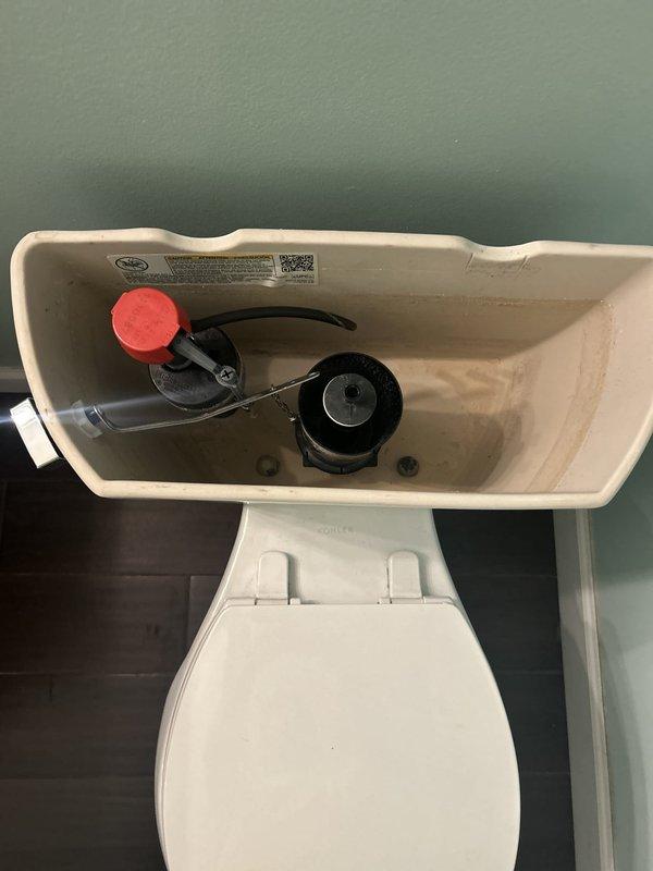 Completed toilet repair by removing tank lid and inspecting internal flush mechanism components. Assessed fill valve assembly with red cap, black rubber flapper valve, and refill tube connections for proper operation. Documented condition of flush valve assembly and verified water supply line connection. All standard toilet tank components were examined and photographed for service records.