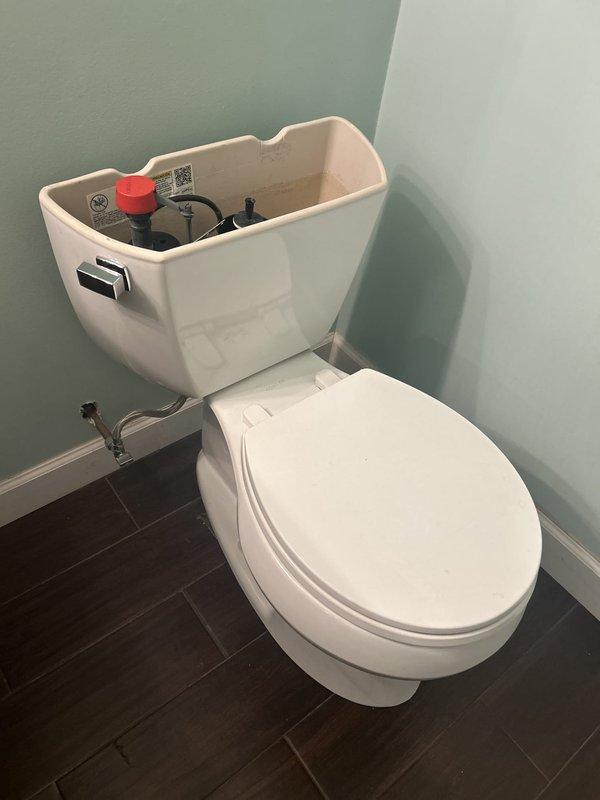 Completed toilet repair by removing tank lid and inspecting internal flush mechanism components. Assessed fill valve assembly with red cap, black rubber flapper valve, and refill tube connections for proper operation. Documented condition of flush valve assembly and verified water supply line connection. All standard toilet tank components were examined and photographed for service records.
