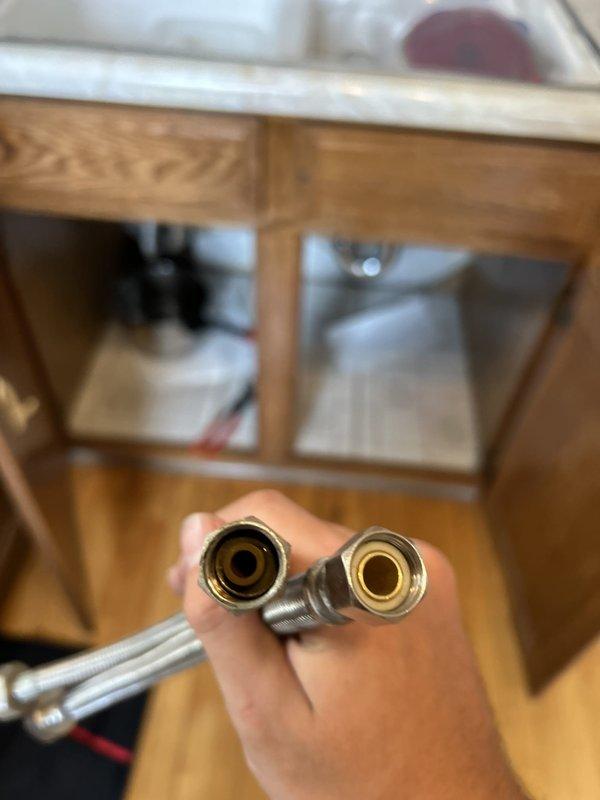 Responded to water leak under kitchen sink originating from supply valve area. Upon inspection, identified failed connection at braided stainless steel supply line fitting installed during previous re-pipe work approximately 2-3 years prior. Shut off water supply and removed defective flexible supply lines with brass fittings. Inspected copper stub-out connections and cabinet interior for additional water damage or deterioration. Replaced both hot and cold water braided supply lines with new assemblies, ensuring proper gasket seating and torque specifications on threaded connections. Tested system under full pressure, verified no leaks at valve connections or fittings, and confirmed proper water flow to fixtures.