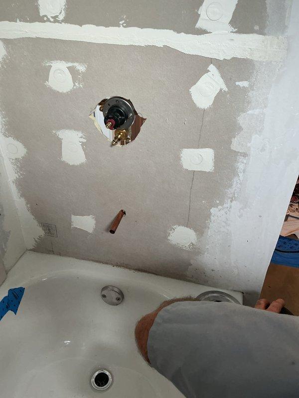 Responded to warranty callback for shower valve installation with improper wall gap. Accessed plumbing through ceiling cavity to assess supply line connections and valve mounting. Performed drywall repair and joint compound application around shower valve trim to eliminate gap and ensure proper wall finish. Documented existing conditions showing exposed valve body, copper supply piping, and unfinished wall surface requiring remediation to complete installation to code standards.
