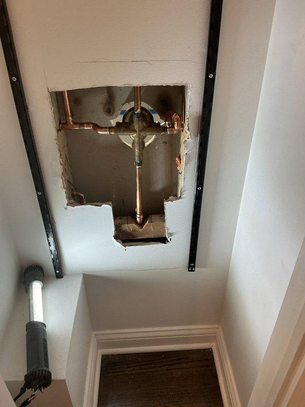 Responded to warranty callback for shower valve installation with improper wall gap. Accessed plumbing through ceiling cavity to assess supply line connections and valve mounting. Performed drywall repair and joint compound application around shower valve trim to eliminate gap and ensure proper wall finish. Documented existing conditions showing exposed valve body, copper supply piping, and unfinished wall surface requiring remediation to complete installation to code standards.