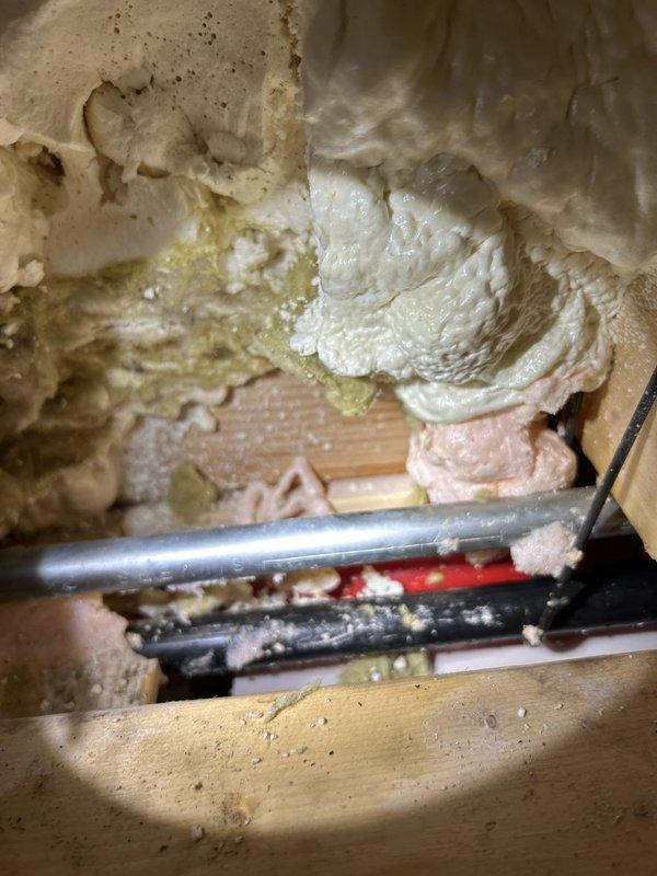 Completed comprehensive drain and sewer system assessment for commercial property, documenting existing infrastructure conditions including pipe routing through structural wall cavities and access points near garage/storage areas. Inspection revealed plumbing lines running through insulated wall sections with spray foam application around drainage components, photographed all accessible pipe configurations and structural penetrations to provide detailed estimate for potential repair or replacement work.
