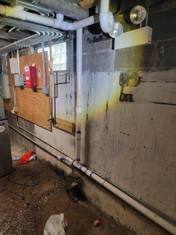 Responded to a plumbing service call at a commercial or multi-unit facility where basement water infiltration and drainage issues were identified. Upon inspection, discovered significant water staining and discoloration on concrete block walls in the utility area, with evidence of ongoing moisture problems affecting the space. Evaluated existing PVC drainage piping system running throughout the basement ceiling and walls to identify potential failure points or blockages contributing to the water damage. Assessed the exterior plumbing infrastructure including ground-level access points and drainage systems near the building foundation to determine the source of water intrusion and recommend appropriate repairs to prevent future basement flooding and structural deterioration.