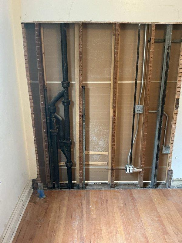Responded to plumbing issue involving cast iron main stack connection to kitchen sink drain. Accessed work area by removing drywall section to expose wall cavity and plumbing infrastructure. Replaced deteriorated cast iron stack connection with new PVC drainage system, including vertical drain pipes and multiple elbow fittings to properly route kitchen sink drain to main stack. Secured all new plumbing components with appropriate hangers and supports to ceiling joists. Verified proper drainage flow and leak-free connections throughout modified system.