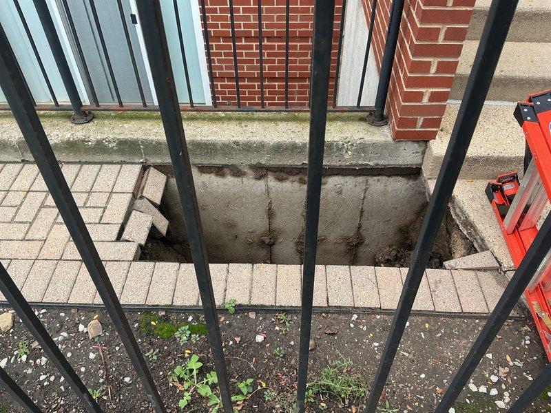 Responded to commercial property for sinkhole assessment in front of building. Upon arrival, identified significant subsurface void that had caused sidewalk collapse near street-level entrance. Sinkhole located adjacent to decorative brick paver border and concrete walkway, creating safety hazard for pedestrian traffic. Area secured with caution tape to prevent public access during evaluation.

Conducted visual inspection revealing deteriorated conditions beneath surface pavement, with evidence of soil erosion and settlement around utility corridor. Documented compromised paving stones and structural integrity issues at building perimeter where foundation meets public walkway. Photographed extent of damage including affected sidewalk sections, tree well areas, and proximity to wrought iron fencing and residential structures.

Prepared comprehensive estimate for drain and sewer line investigation, including camera inspection to determine if failed underground infrastructure contributed 