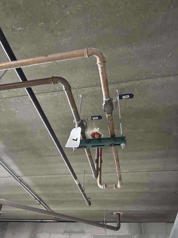 Returned to property to document hot water main piping system with photographs for estimate preparation. Photographed ceiling-mounted copper piping assembly including main shut-off valves, flow control devices, and pipe routing in mechanical space. Images captured condition of existing copper lines showing oxidation and age-related deterioration, valve locations with identification tags, and support bracket configurations for condo association review and repair approval process.