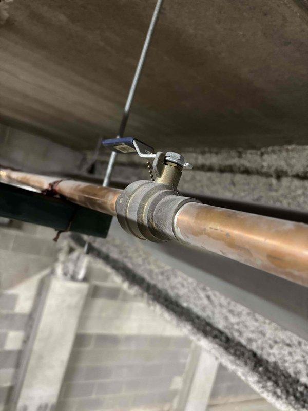 Returned to property to document hot water main piping system with photographs for estimate preparation. Photographed ceiling-mounted copper piping assembly including main shut-off valves, flow control devices, and pipe routing in mechanical space. Images captured condition of existing copper lines showing oxidation and age-related deterioration, valve locations with identification tags, and support bracket configurations for condo association review and repair approval process.