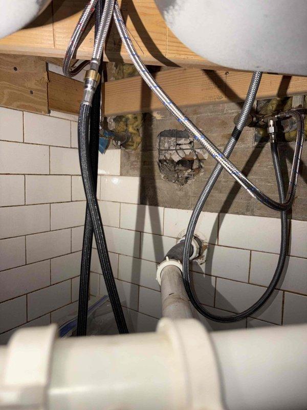 Responded to a rescheduled priority service call for a reported slow leak at the kitchen faucet. Upon arrival, conducted a thorough inspection of the kitchen sink area, including the double-basin stainless steel sink and tall brushed nickel faucet assembly. Traced water supply lines from the kitchen fixture down to the water heater connections to identify the source of the leak. Inspected flexible braided metal supply lines and connections at the water heater, examining both the hot and cold water feeds. Identified leak source and assessed condition of supply line connections, mounting hardware, and surrounding plumbing infrastructure. Documented existing conditions with photographs showing the kitchen faucet installation and the water supply routing through the wooden framing to the water heater. Completed leak location service and provided findings to customer regarding the source of the reported slow leak condition.