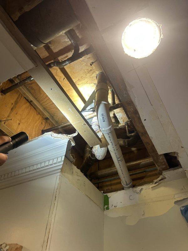 Responded to a bathtub leak affecting the unit below. Upon inspection, identified the source of water intrusion by examining the tub drain assembly and overflow connections. Accessed the plumbing system from below through the ceiling of the lower unit to assess pipe connections and identify the leak point. Inspected exposed PVC drainage piping and verified proper pitch and connections. Documented existing conditions including incomplete shower valve installation with exposed rough-in plumbing at the wall. Tightened drain connections and tested the system to confirm leak resolution.