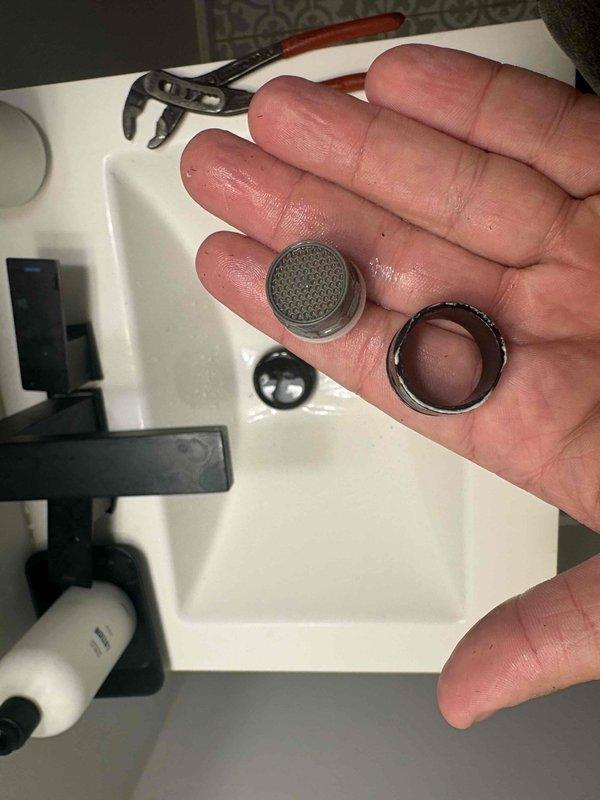 Responded to low water pressure complaint at residential bathroom sink. Upon inspection, identified clogged faucet aerator as the source of reduced flow. Removed aerator assembly from waterfall-style black matte faucet using adjustable wrench. Disassembled aerator components, including mesh screen and retaining ring, which showed significant sediment and mineral buildup restricting water flow. Cleaned all aerator parts thoroughly, reassembled components, and reinstalled onto faucet. Tested water pressure after service and confirmed restoration to normal flow rate.