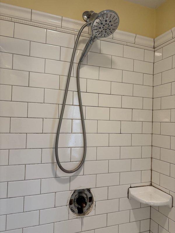 Responded to warranty callback for recently installed shower valve experiencing leaking and temperature control issues. Upon arrival, inspected chrome shower valve assembly with handheld showerhead system mounted on white subway tile wall. Customer reported valve was only delivering hot water and had developed a leak following initial installation. Diagnosed faulty cartridge installation in single-lever mixing valve. Removed escutcheon plate and accessed valve body to inspect cartridge seating and orientation. Corrected cartridge positioning to restore proper hot/cold water mixing function. Tested temperature control through full range of motion to verify balanced water delivery. Addressed leak source at valve connection points, tightened compression fittings, and verified all seals were properly seated. Cycled valve multiple times to confirm leak resolution and proper temperature regulation from cold to hot settings. System now operating within manufacturer specifications with no acti