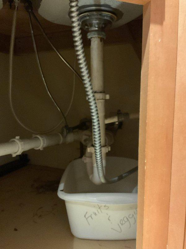 Conducted on-site assessment for kitchen sink and faucet replacement in tenant unit. Inspected existing stainless steel double-basin sink with chrome single-handle faucet and side spray assembly. Examined undersink plumbing configuration including drain assembly with gray metal tailpiece, flexible braided supply lines, and white PVC drain piping. Identified active leak beneath sink requiring immediate attention. Documented current fixture conditions and cabinet access points. Provided estimate for budget-friendly replacement options for sink and faucet assembly, along with repair of identified leak in undersink plumbing system.