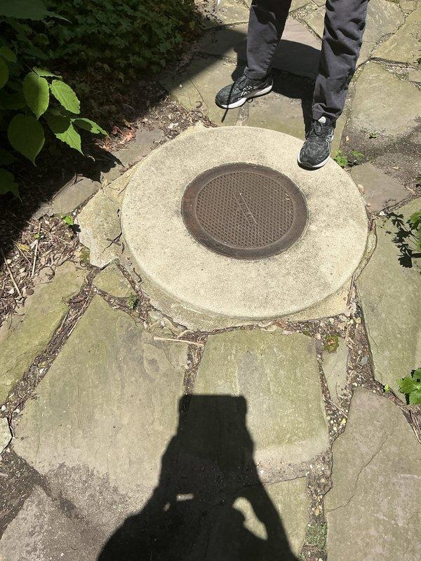 Completed follow-up visit to collect down payment for previously sold sewer cleanout cover replacement repair. Documented existing weathered circular metal access cover with perforated surface and corroded lifting mechanism set in concrete pad within flagstone patio area, confirming scope of work for upcoming installation.