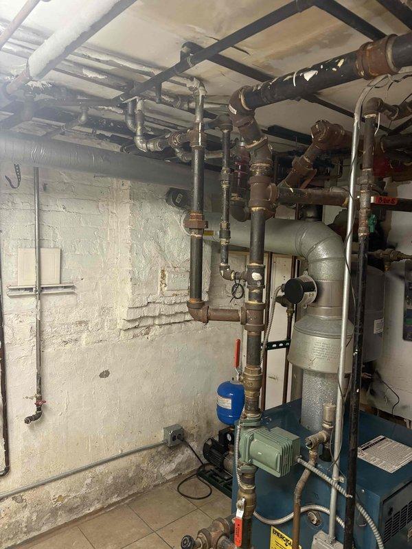 # Plumbing System Repair and Wall Access

Completed emergency plumbing repair requiring structural wall access to reach concealed piping system. Demolished section of tiled bathroom wall to expose internal plumbing infrastructure and address critical leak or system failure. Removed damaged drywall, tile sections, and wall materials to create access opening revealing wooden stud framing and vertical utility conduits.

Accessed basement mechanical room housing water heater, boiler system, and primary distribution piping network. Inspected and repaired plumbing connections, valves, and pressure regulation components within the multi-system configuration. Work involved coordination with existing heating equipment, water supply lines, and pressure tank assembly.

Repair services sold with financing arrangement. Customer scheduled for follow-up coordination to complete wall restoration and finish work. Documented pre-repair conditions and mechanical room configuration with photographic recor