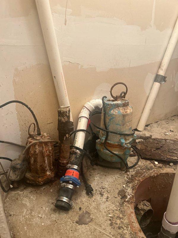 Completed comprehensive assessment of existing dual sump pump system showing extensive deterioration and operational concerns. Both pumps exhibited severe corrosion, rust damage, and paint degradation consistent with prolonged moisture exposure and age-related failure. The primary pump displayed heavy rust throughout the casing and metal components, while the secondary backup pump showed significant paint flaking and corrosion spots. Evaluated the sump pit configuration, which contained standing water and deteriorated concrete surfaces with substantial sediment accumulation. Inspected white PVC discharge piping assembly including check valve and backflow preventer connections. Documented floor staining, debris buildup, and wall discoloration indicating chronic moisture issues and inadequate drainage management. Provided detailed estimate for complete sump pump system replacement including removal of both failed units, pit cleaning, installation of new primary and backup pump units with