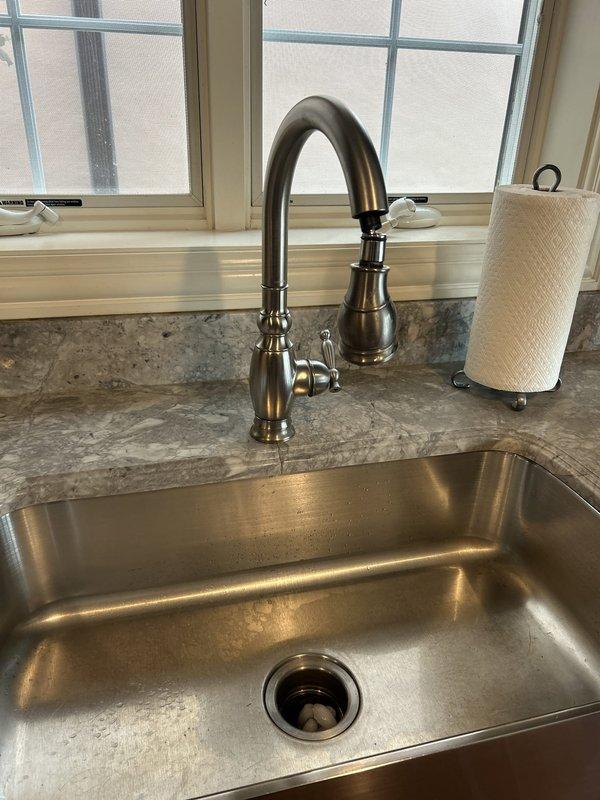 Successfully replaced existing kitchen faucet with new single-hole faucet and integrated pull-down sprayer assembly. Removed old brushed nickel gooseneck faucet with side handle and installed modern chrome pull-down faucet featuring coiled spout design. Verified proper water supply line connections, tested hot and cold water flow, confirmed sprayer functionality, and inspected for leaks at all connection points.