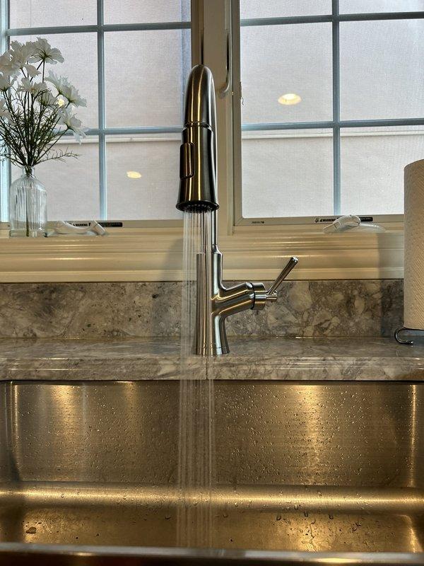 Successfully replaced existing kitchen faucet with new single-hole faucet and integrated pull-down sprayer assembly. Removed old brushed nickel gooseneck faucet with side handle and installed modern chrome pull-down faucet featuring coiled spout design. Verified proper water supply line connections, tested hot and cold water flow, confirmed sprayer functionality, and inspected for leaks at all connection points.