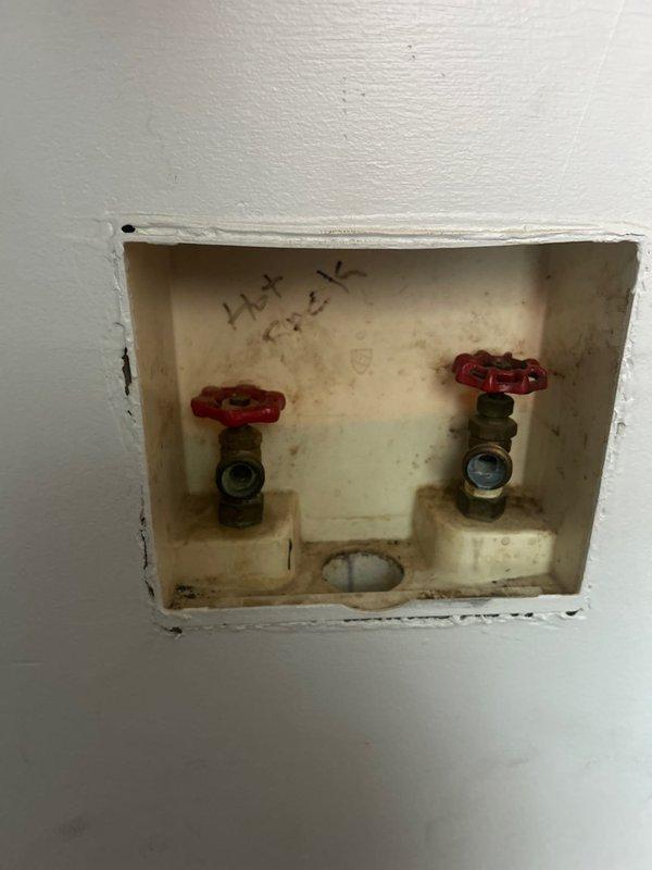 Installed gas line plumbing for dryer connection and completed drain plumbing infrastructure for washer appliance. Work included installation of dual shut-off valves with manual wheel handles in recessed wall access box, along with white PVC drain line configuration featuring 90-degree elbows and cleanout access point positioned at floor level in corner installation.