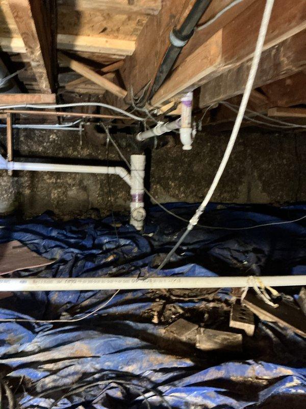 Inspected crawl space to investigate reported leaking from outdoor spigot that had been recently replaced but was surrounded by concrete. Accessed underfloor area and examined plumbing infrastructure, vapor barrier integrity, and foundation walls for signs of water intrusion. Documented existing conditions including PVC piping, insulation, electrical wiring, and moisture indicators on foundation surfaces to assess potential leak source and water damage.