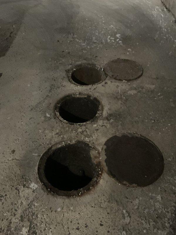 Responded to service call for catch basin maintenance and inspection. Upon arrival, accessed multiple catch basin openings in concrete floor to assess drainage system condition. Removed covers from several catch basins to inspect for blockages and debris accumulation that could be causing backup issues. Performed thorough cleaning of catch basins, removing sediment, debris, and buildup from basin interiors. Inspected connecting pipes and drainage lines for obstructions or flow restrictions. Documented pre-service and post-service conditions with photographs showing basin locations and access points. All catch basins cleaned and verified for proper drainage function before replacing covers and completing service.