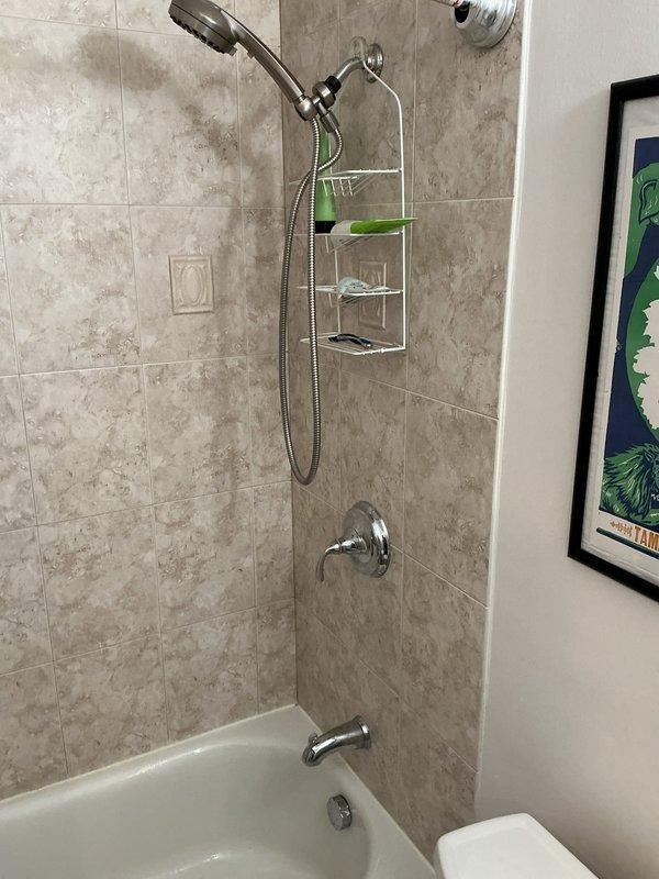 Responded to service call for leaking bathtub faucet in residential bathroom with alcove-style tub/shower combination. Upon inspection, documented existing chrome tub spout and shower valve system with handheld and fixed showerhead configuration installed on beige marble-pattern tiled surround. Photographed current fixture conditions and plumbing layout for assessment and estimate preparation, with follow-up appointment scheduled to complete necessary repairs.