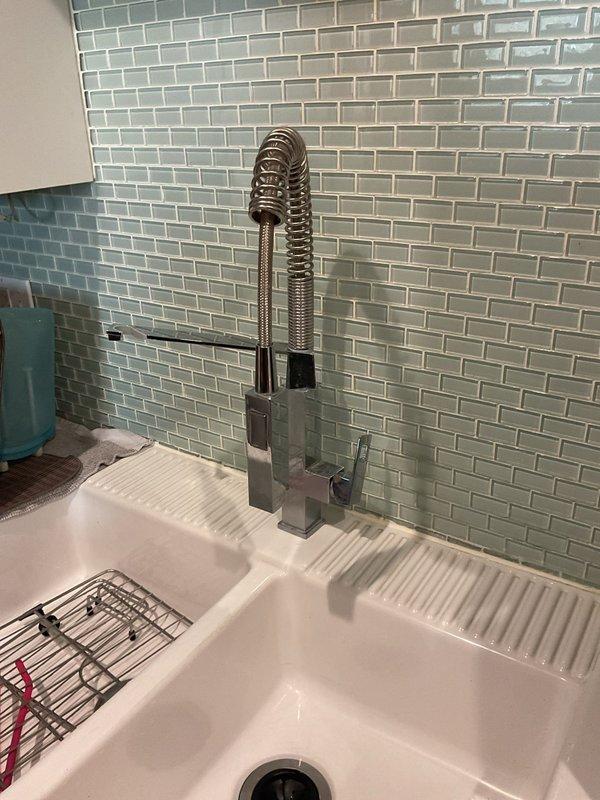 Installed customer-supplied chrome pull-down kitchen faucet with commercial-style coiled spring design at white farmhouse sink. Connected water supply lines to existing copper plumbing infrastructure and verified proper operation of spray function and handle controls, ensuring no leaks at all connection points.