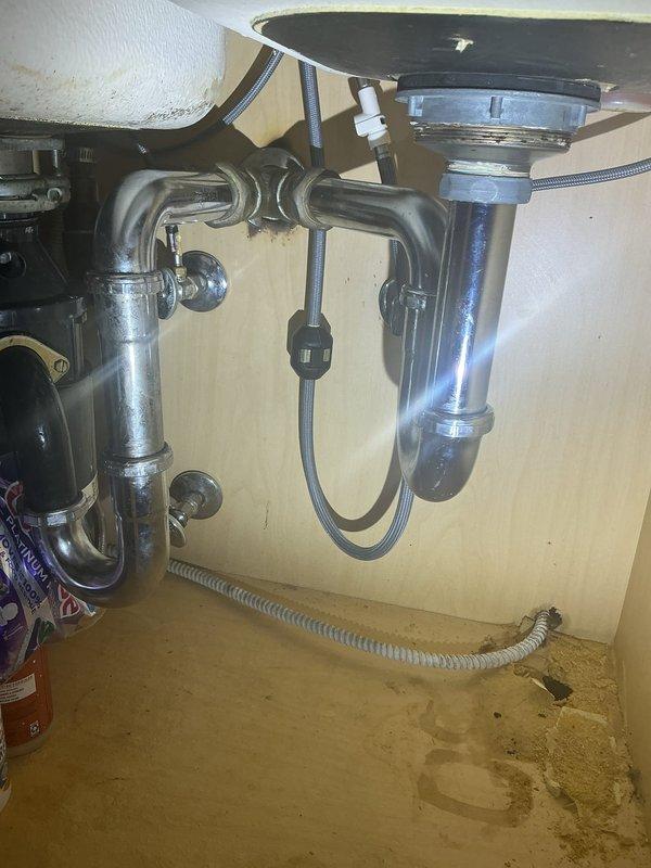 Completed installation of kitchen sink drain assembly and P-trap configuration beneath stainless steel sink basin. Installed chrome-finished P-trap piping with proper curved sections connecting sink drain to wall outlet, ensuring adequate water seal and proper drainage flow. Connected garbage disposal unit to drain system with appropriate fittings and flexible supply lines for optimal functionality.