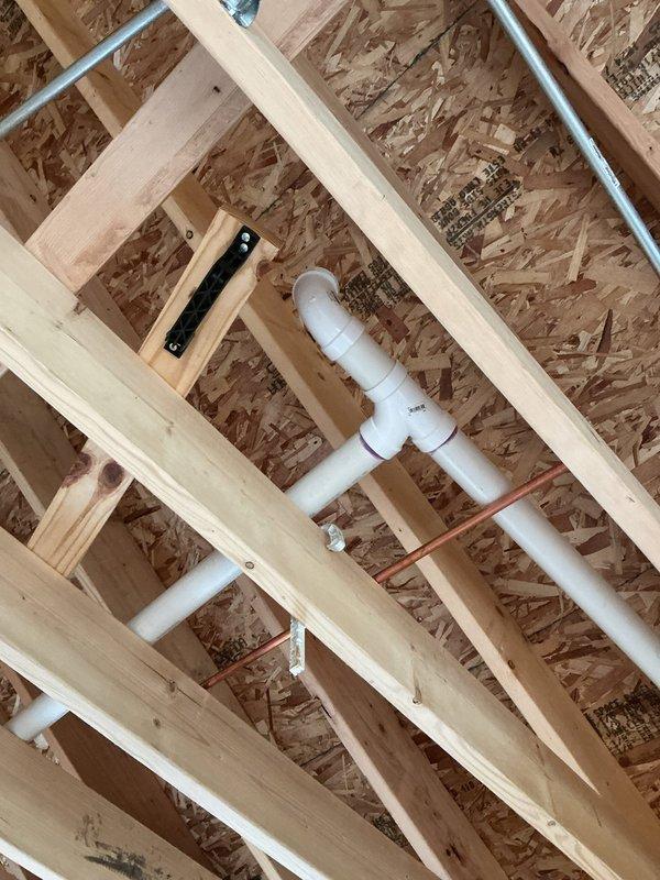 Completed comprehensive home plumbing inspection of new construction property, documenting rough-in plumbing installation including white PVC drainage and venting system running through exposed ceiling joists and OSB sheathing. Reviewed construction notes and permit documentation, photographed plumbing configuration with elbows and straight runs for approval process, and identified that technician needs to return for follow-up assessment of required repairs or modifications.