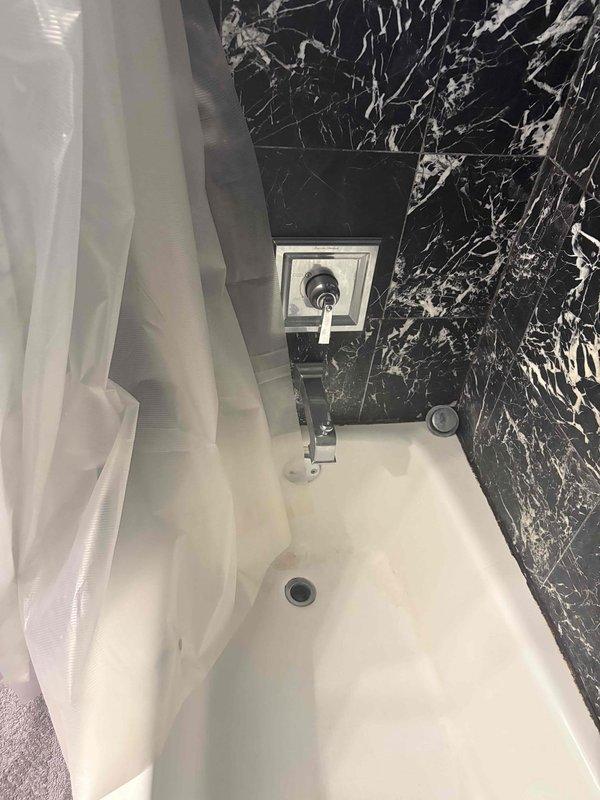 Completed plumbing repair consultation and assessment for bathroom fixtures in residential property. Inspected chrome faucet and showerhead assembly mounted above white bathtub with visible chrome drain components. Documented existing bathroom configuration featuring bathtub installation against black marble-patterned wall surround with white veining, and evaluated plumbing fixture conditions for repair recommendations and deposit collection.