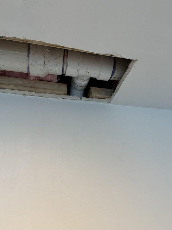 Completed plumbing repair involving ceiling access to drainage system. Created access openings in ceiling to expose PVC drain and vent piping for inspection and repair work. Addressed plumbing issues with horizontal drain line and vertical vent stack, including work on elbow joint connections. Ceiling panels were removed to provide necessary access to wooden framing and plumbing infrastructure above.