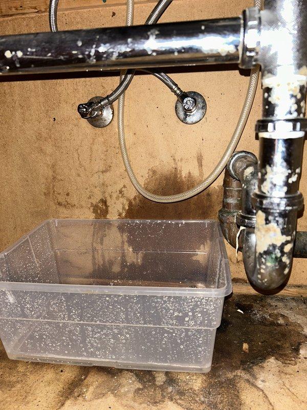 Responded to water leak complaint originating from second-floor sink with water intrusion into downstairs bathroom. Upon investigation, located active leak at sink drain assembly and supply line connections. Documented extensive water staining on wall surfaces and surrounding areas indicating prolonged moisture exposure. Found P-trap assembly showing signs of deterioration and compromised seals. Placed collection containers beneath affected plumbing to manage active dripping while assessing damage. Identified multiple potential leak sources including corroded shutoff valves, aged braided supply lines, and deteriorated drain connections. Photographed all affected areas showing water damage patterns, stained flooring, and compromised plumbing fixtures for documentation purposes.