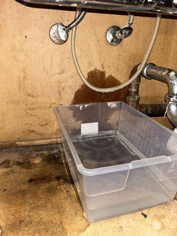 Responded to water leak complaint originating from second-floor sink with water intrusion into downstairs bathroom. Upon investigation, located active leak at sink drain assembly and supply line connections. Documented extensive water staining on wall surfaces and surrounding areas indicating prolonged moisture exposure. Found P-trap assembly showing signs of deterioration and compromised seals. Placed collection containers beneath affected plumbing to manage active dripping while assessing damage. Identified multiple potential leak sources including corroded shutoff valves, aged braided supply lines, and deteriorated drain connections. Photographed all affected areas showing water damage patterns, stained flooring, and compromised plumbing fixtures for documentation purposes.