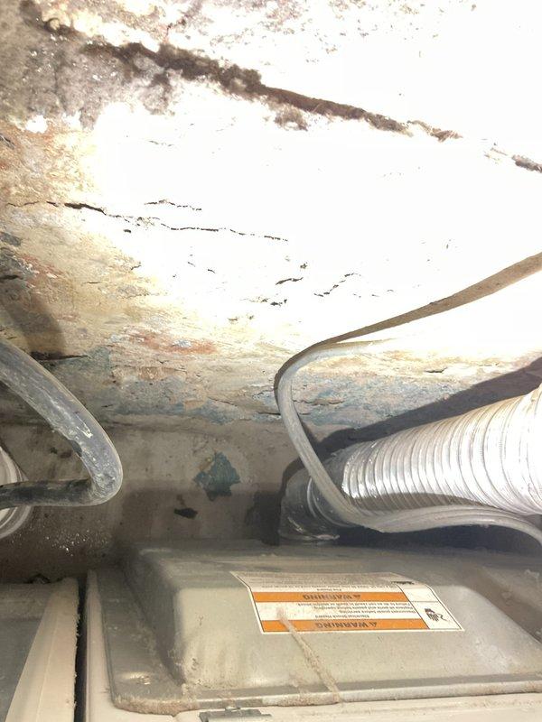 Responded to service call for dryer connection in basement laundry area. Upon arrival, assessed existing laundry setup with white dryer and washing machine positioned against green painted wall. Inspected flexible aluminum ductwork for dryer exhaust venting system and verified proper routing from appliance to exterior vent. Examined electrical connections and PVC plumbing infrastructure servicing the laundry appliances. Noted deteriorated ceiling conditions in adjacent garage area showing moisture damage, paint deterioration, and staining on overhead surfaces near mechanical components. Scheduled follow-up visit to complete final dryer hookup and connection to ensure proper venting and electrical service for safe appliance operation.