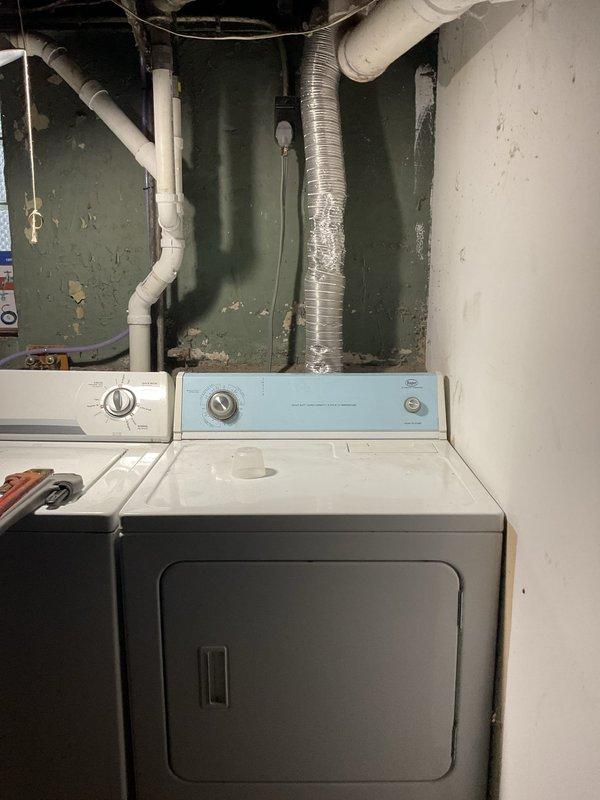 Responded to service call for dryer connection in basement laundry area. Upon arrival, assessed existing laundry setup with white dryer and washing machine positioned against green painted wall. Inspected flexible aluminum ductwork for dryer exhaust venting system and verified proper routing from appliance to exterior vent. Examined electrical connections and PVC plumbing infrastructure servicing the laundry appliances. Noted deteriorated ceiling conditions in adjacent garage area showing moisture damage, paint deterioration, and staining on overhead surfaces near mechanical components. Scheduled follow-up visit to complete final dryer hookup and connection to ensure proper venting and electrical service for safe appliance operation.