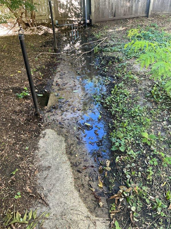 Responded to service call for water line leak causing significant flooding in backyard. Upon arrival, identified compromised main water line resulting in substantial water accumulation throughout the yard. Inspected interior utility area and water meter installation, noting aging galvanized piping system with visible corrosion and mineral deposits. Assessed exterior conditions revealing saturated ground with standing water pooled along property line near wooden fence. Excavated and exposed damaged section of main water line. Replaced compromised pipe segment with new materials, ensuring proper connections and secure fittings. Tested system for leaks and verified proper water flow and pressure at meter. Backfilled excavation area and restored ground surface. System returned to full operational status with no active leaks detected.