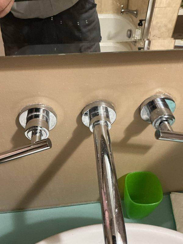 Completed installation of wall-mounted, three-piece chrome faucet assembly with center spout and dual lever handles for modern vessel sink in residential bathroom. All fixtures properly mounted, sealed, and tested for proper water flow and temperature control with no leaks detected.