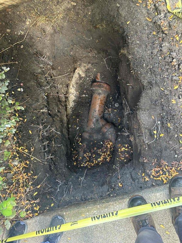 Responded to residential property for drain and sewer system evaluation. Upon arrival, observed recent concrete pathway repair work with caution tape perimeter indicating active curing process in landscaped front yard area. Conducted thorough inspection of underground plumbing infrastructure, which revealed severely corroded cast iron pipe fitting requiring replacement. Excavated and exposed deteriorated piping component showing extensive rust damage and structural compromise from prolonged moisture exposure and age-related degradation. Documented existing conditions through photographic evidence of both surface-level concrete work and subsurface plumbing failures. Assessed scope of necessary repairs including removal of compromised piping sections and installation of updated drain and sewer line components. Prepared comprehensive estimate for complete pipe replacement, excavation requirements, and restoration of affected landscape and hardscape areas following completion of undergroun