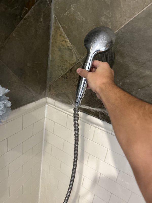 Responded to service call for leaking shower hose in residential bathroom. Upon inspection, assessed handheld shower assembly mounted on chrome slide bar rail system installed over diagonal slate tile wall. Examined flexible metal hose connection points at both the wall-mounted diverter valve and handheld shower head fixture for signs of wear, deterioration, or improper sealing. Evaluated hose integrity along entire length and tested connections under water pressure to identify source of leak. Inspected mounting hardware, slide bar brackets, and wall-mounted control valve for proper installation and function. Documented existing conditions of shower fixture assembly and tile surround, noting natural mineral deposits and water staining typical of slate material in wet environment. Photographed shower head, flexible hose, rail system, and surrounding tilework for service records.