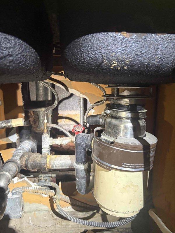 Responded to water intrusion complaint originating from unit above. Upon arrival, conducted thorough inspection of affected condo unit's plumbing systems and water heater installation. Examined A.O. Smith household storage tank water heater (Model AD040009488, Serial R2612877005) rated at 240V, 4500W for signs of leakage or failure. Inspected under-sink plumbing assembly including garbage disposal unit, P-trap configuration, and associated drain connections. Identified significant condensation buildup on insulated supply pipes beneath sink, with extensive moisture accumulation on grey-blue insulated horizontal pipe runs. Assessed all visible plumbing fixtures, connections, and fittings for active leaks or water damage. Documented conditions with photographic evidence showing water heater specifications and under-sink plumbing components. Determined that condensation on cold water supply lines was contributing to localized moisture but confirmed leak source required coordination with up