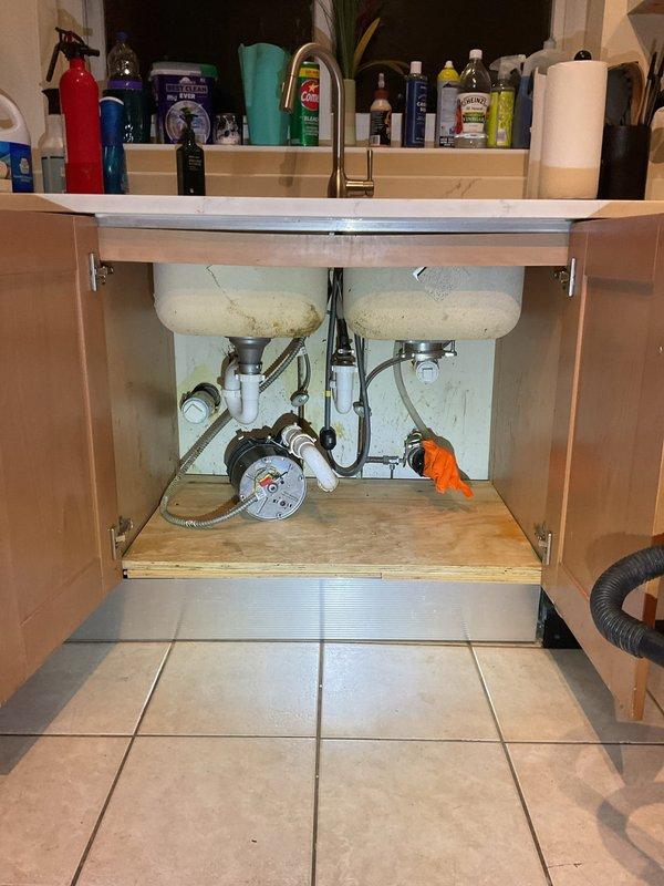 Responded to a persistent kitchen sink drainage issue that began following grease trap removal and garbage disposal replacement. Upon arrival, found double-basin sink with newly installed disposal unit that remained non-functional despite previous 30-foot cable rodding attempts by another contractor. Inspected under-sink plumbing configuration including PVC P-traps, drain assemblies, and disposal connections. Identified blockage or improper drainage pathway downstream of disposal unit that was not resolved by standard augering methods. Cleared obstruction and restored proper drainage flow to both sink basins. Tested system operation with disposal running and water flowing through both basins to verify complete resolution. Photographed completed plumbing configuration showing proper P-trap installation, disposal connections, and supply line routing for service documentation.