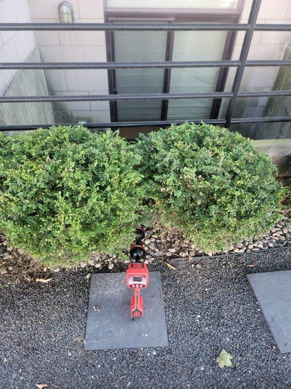 Installed new backflow prevention valve in exterior landscaped area. Device was mounted on paver surface among decorative rock bed near building foundation with metal railing system. Valve assembly features red body with black control components for proper water flow regulation and cross-connection protection.