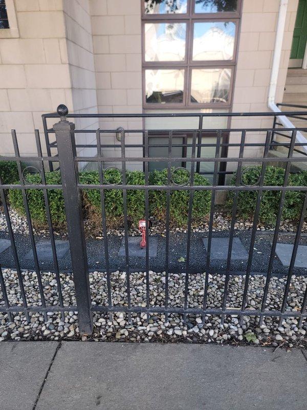 Installed new backflow prevention valve in exterior landscaped area. Device was mounted on paver surface among decorative rock bed near building foundation with metal railing system. Valve assembly features red body with black control components for proper water flow regulation and cross-connection protection.